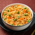 Schezwan Noodles or vegetable Hakka Noodles or chow mein, served in a bowl or plate with tomato sauce, ketchup, wooden chopsticks, India. popular Indo-Chinese Indian Maggi noodles.