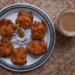 Top view of Dal vada, masala vada, chana vada served with cut onion and green chilly and Tea on serving mat. Deep fried indian cuisine snacks, lentils, pulses fritters